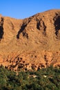 Panoramic view over palm grove oasis on isolated clay house village, rugged steep limestone mountain face background