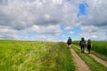 Panoramic view of people hiking on a road near a green field under a cloudy blue sky Royalty Free Stock Photo