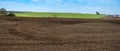 Panoramic view of plowed field with furrows and traces of tractor tires near green field.