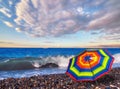 Rainbow umbrella on summer beach of tropical sea with azure waves and white ship under dramatic cloudy sky Royalty Free Stock Photo