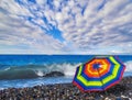 Rainbow umbrella on summer beach of tropical sea with azure waves and white ship under dramatic cloudy sky Royalty Free Stock Photo