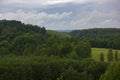 Panoramic view of rolling green hills and dense forest under dramatic cloudy summer sky Royalty Free Stock Photo