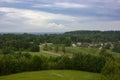 Panoramic view of rural village surrounded by lush green forests and rolling fields under dramatic cloudy summer sky Royalty Free Stock Photo
