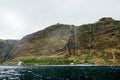 Panoramic view of sheer volcanic cliff rising above ocean.