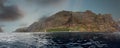 Panoramic view of sheer volcanic cliff rising above ocean.