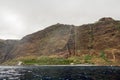 Panoramic view of sheer volcanic cliff rising above ocean.