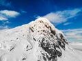 Panoramic view of a snow capped mountain peak with clouds and blue skies.