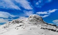 Panoramic view of a snow capped mountain peak with clouds and blue skies.