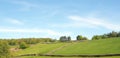 panoramic view of sunlit summer countryside with green rolling hilly meadows surrounded by stone walls and forest trees above Royalty Free Stock Photo