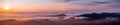 Panoramic view of a sunset over a sea of clouds covering south San Francisco bay area; mountain ridges in the foreground; view