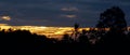 Panoramic view of sunset ray with clouds in sky and silhouette of landscape foreground Royalty Free Stock Photo