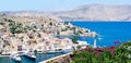 Panoramic view on tiny colorful houses on rocks and big boats on harbor near the Mediterranian sea on Greek island in sunny summer
