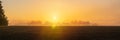 Panoramic view to tree silhouette on agriculture field with misty fog and sunbeam. Gold colored sunrise, Czech landscape