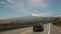 Panoramic view of vehicles driving on the road with the Cayambe volcano in the background during a sunny day with blue sky