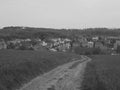 Blackwhite image - Panoramic view on a village with multicolored houses behind a field with a dirt road in the right middle and fo