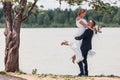Panoramic view at young couple bride in white and groom in blue standing among lake under a branch of green tree, posing and Royalty Free Stock Photo