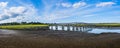 Panoramic vistas of long wooden bridge stretching across green swamp and river under big blue sky with white clouds Royalty Free Stock Photo