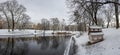 Panoramic winter landscape with snow in park with canal in Riga, Latvia. View of small house for birds snow covered park