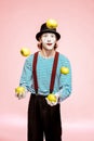 Pantomime juggling with apples on the pink background