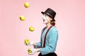 Pantomime juggling with apples on the pink background