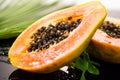 Papaya fruit on tropical palm tree leaf background macro shot. Halved fresh organic Papayas