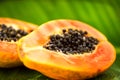 Papaya fruit on tropical palm tree leaf background macro shot. Halved fresh organic Papayas