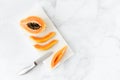 Papaya Half and Slices on White Marble Board with Knife