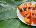 Papaya and passion fruit pieces on white plate with green banana leaves background, copy space Royalty Free Stock Photo