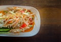 Papaya salad cooked with cowpea, peanut, carrot, lemon, chilis and sugar on white plate food long beans Wood Table Texture.