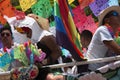 Among papel picado protesters of the LGBTTTI pride march ride on allegorical car adorned with rainbow colors wearing hats and sun