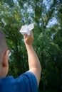 Paper airplane in children hands on greenery background and blue sky in sunny summer day. Concept of summer, childhood, dreaming. Royalty Free Stock Photo