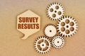 On a paper background, gears and a thought plate with the inscription - Survey Results