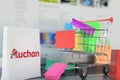 Paper bag with Auchan logo and shopping cart on a laptop keyboard. Editorial online shopping related 3D rendering