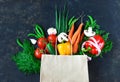 Paper bag with fresh vegetables on a dark background: tomato, zucchini, onion, lettuce, dill, pepper, cucumber, garlic Royalty Free Stock Photo