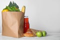 Paper bag with fresh vegetables and other products on wooden table against light background, space for text Royalty Free Stock Photo