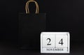 Paper bag and November 24 on a wooden calendar, black background. Black Friday