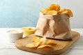 Paper bag of potato chips. Beer snacks, sauce on cutting board, on white wooden background Royalty Free Stock Photo