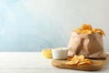 Paper bag of potato chips. Beer snacks, sauce on cutting board, on white wooden background Royalty Free Stock Photo