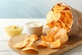 Paper bag of potato chips. Beer snacks, sauce on cutting board, on white wooden background, space for text Royalty Free Stock Photo