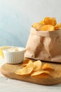 Paper bag of potato chips. Beer snacks, sauce on cutting board, on white wooden background, space for text Royalty Free Stock Photo