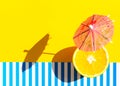 Paper beverage umbrella fresh juicy orange on bright yellow blue and white striped background. Harsh light hard shadow. Trendy Royalty Free Stock Photo