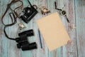 Paper blank, a blue pencil, an old camera, binoculars and compass, sea shells on a light blue wooden background. Royalty Free Stock Photo