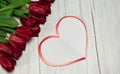 Paper blank in the form of a heart and a spring bouquet of red tulips on a light wooden background. Royalty Free Stock Photo