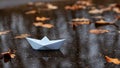 Paper boat floating on the water of an autumn puddle among fallen leaves. Royalty Free Stock Photo