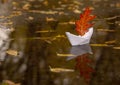 A paper boat floats in a puddle, instead of a sail it has a red oak autumn leaf Royalty Free Stock Photo