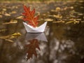 A paper boat floats in a puddle, instead of a sail it has a red oak autumn leaf Royalty Free Stock Photo