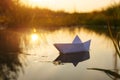 A paper boat floats on the water at dawn.