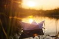 A paper boat floats on the water at dawn.