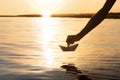 The paper boat goes on a big voyage at sunset, the boy`s hand launches the origami ship on the water