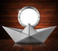 Paper Boat inside a Wooden Ship with Empty Metal Porthole Royalty Free Stock Photo